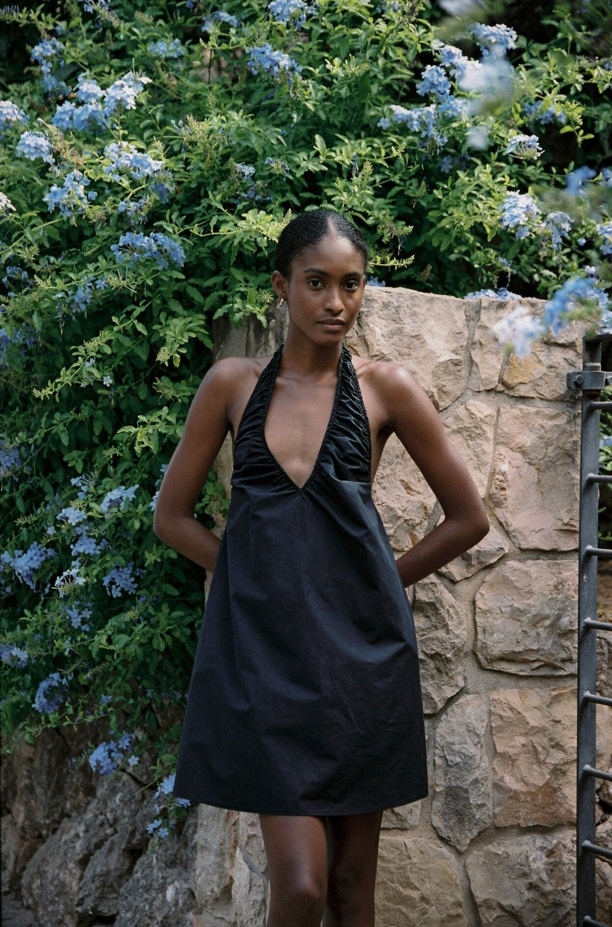 Model wearing the AUDĒRE. Azura cotton halter mini dress in Black, front view of the gathered halter neckline.
