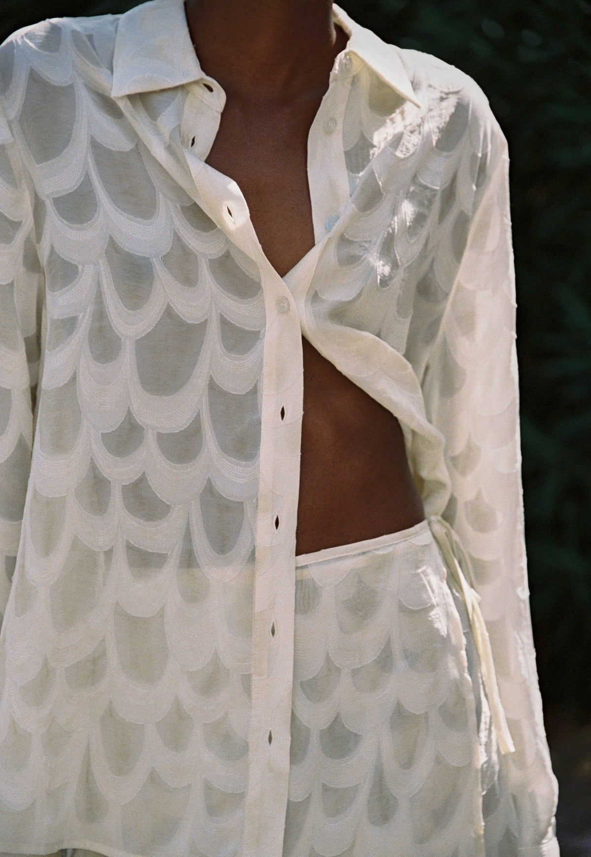 Model wearing the AUDĒRE. Rae semi-sheer shirt in Ivory, close-up of the collar, placket and textured fabric.