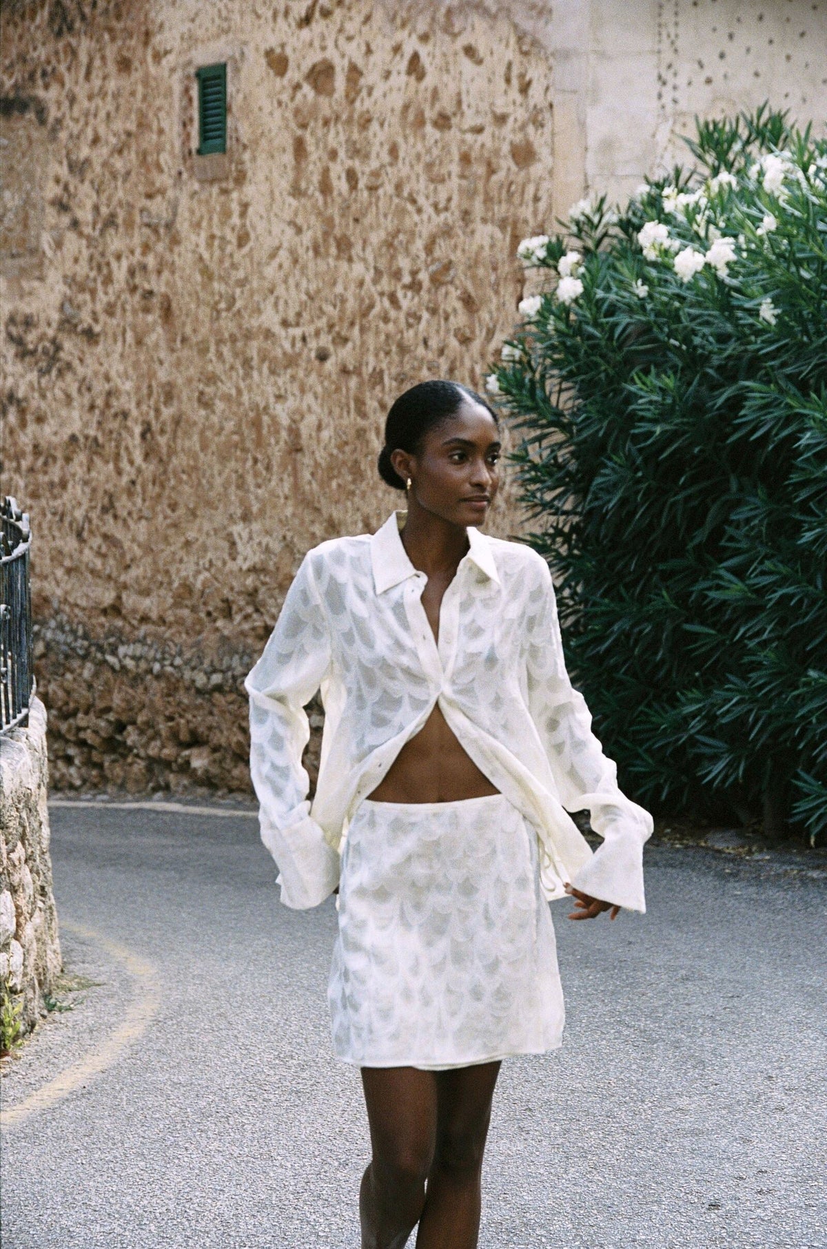 Model wearing the AUDĒRE. Rae wrap mini skirt in Ivory, front view in a village lane.