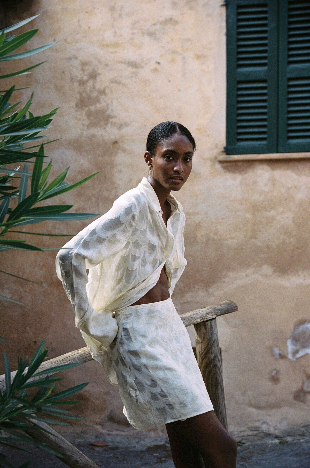 Model wearing the AUDĒRE. Rae wrap mini skirt in Ivory, side view beside a stone stairway.