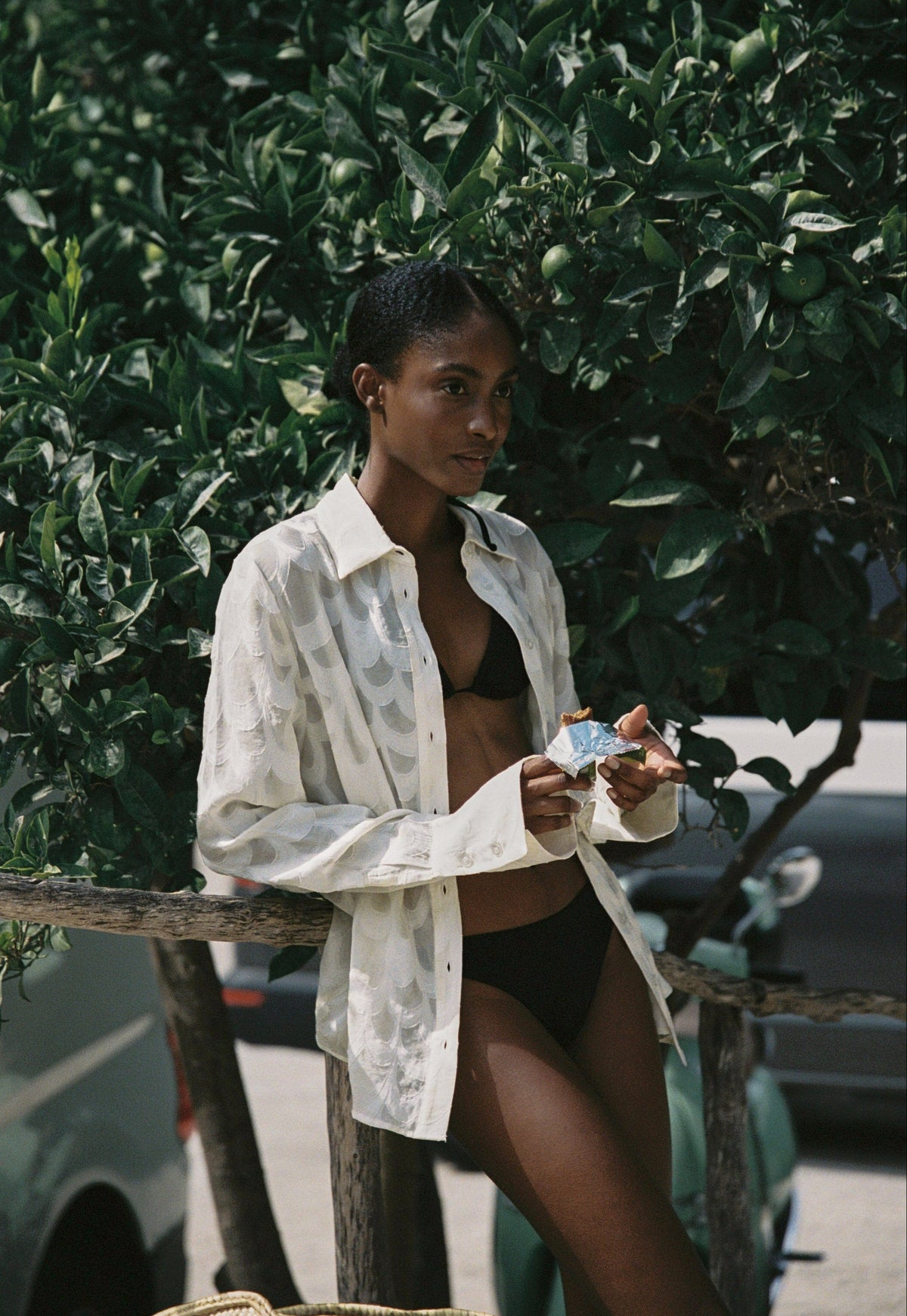 Model wearing the AUDĒRE. Rae semi-sheer shirt in Ivory, seated beside a doorway with a book.