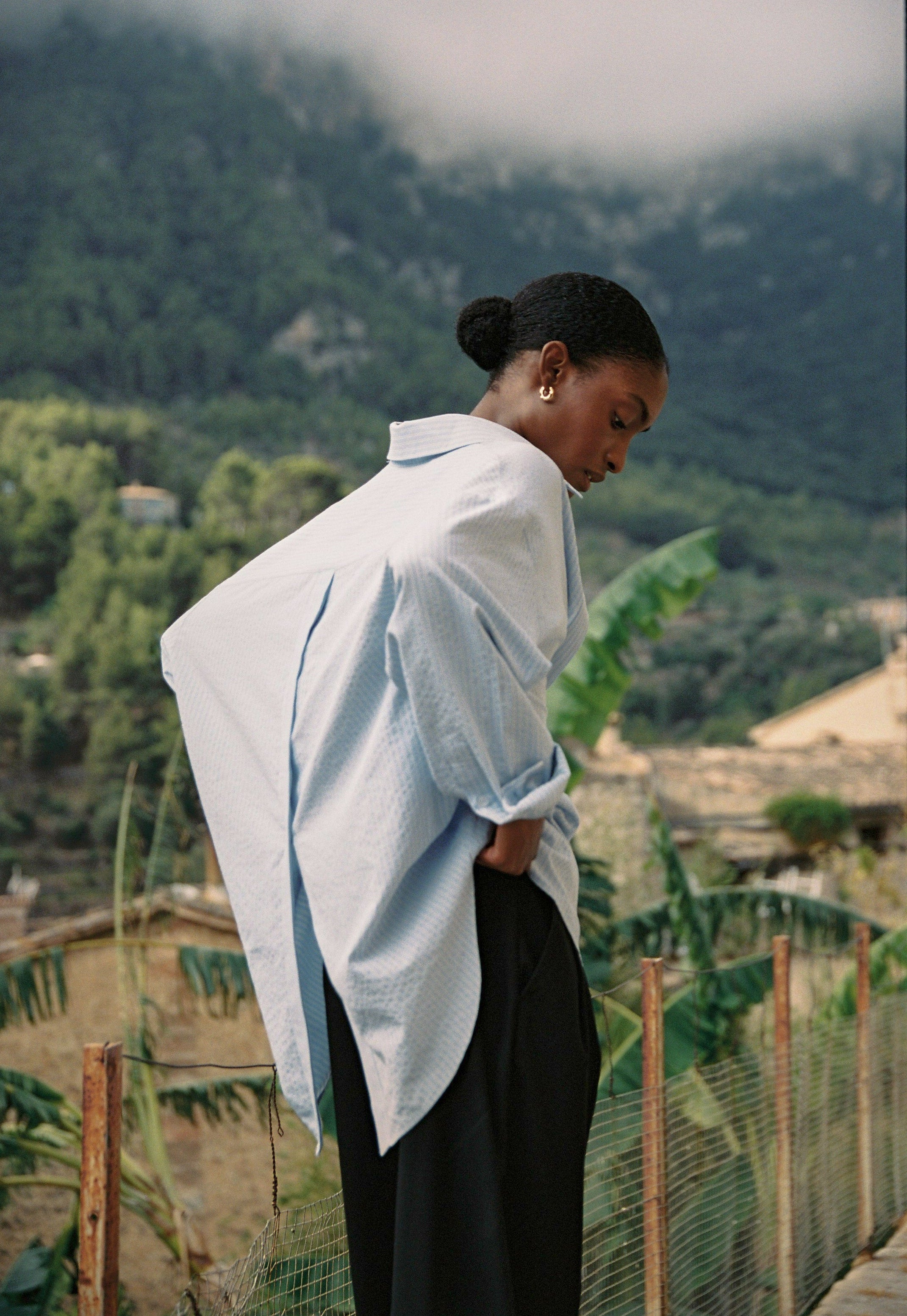 Model wearing the AUDĒRE. Alba oversized striped shirt in Ciel blue, back view of the button-through opening.