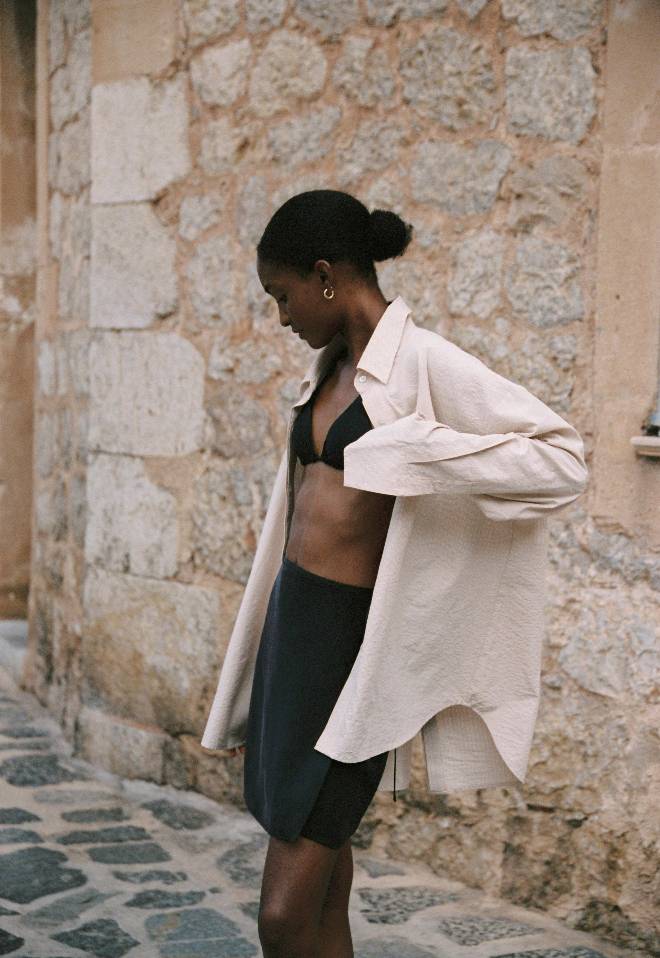 Model wearing the AUDĒRE. Alba oversized shirt in Dune Stripe with the Vero black wrap mini skirt and a black bralette.