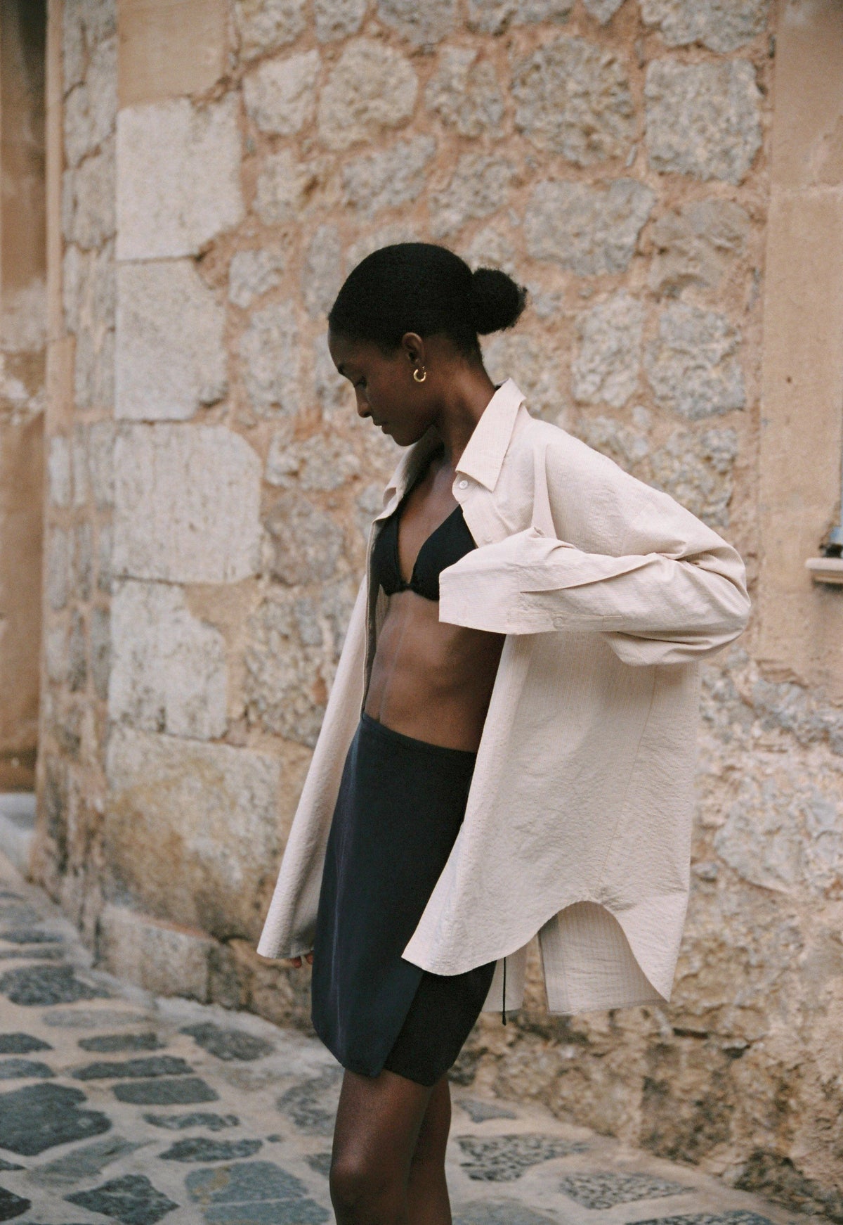 Model wearing the AUDĒRE. Alba oversized shirt in Dune Stripe with the Vero black wrap mini skirt and a black bralette.