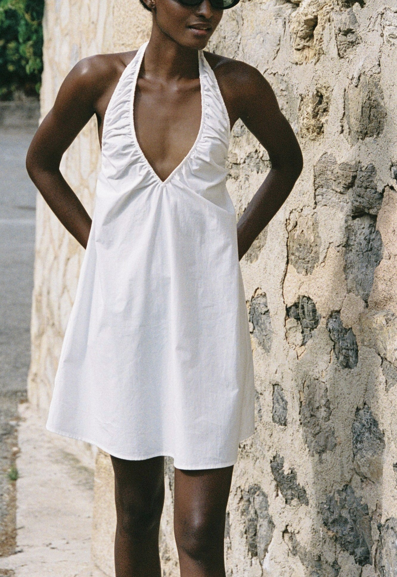 Model wearing the AUDĒRE. Azura cotton halter mini dress in White, close-up of the halter neckline.