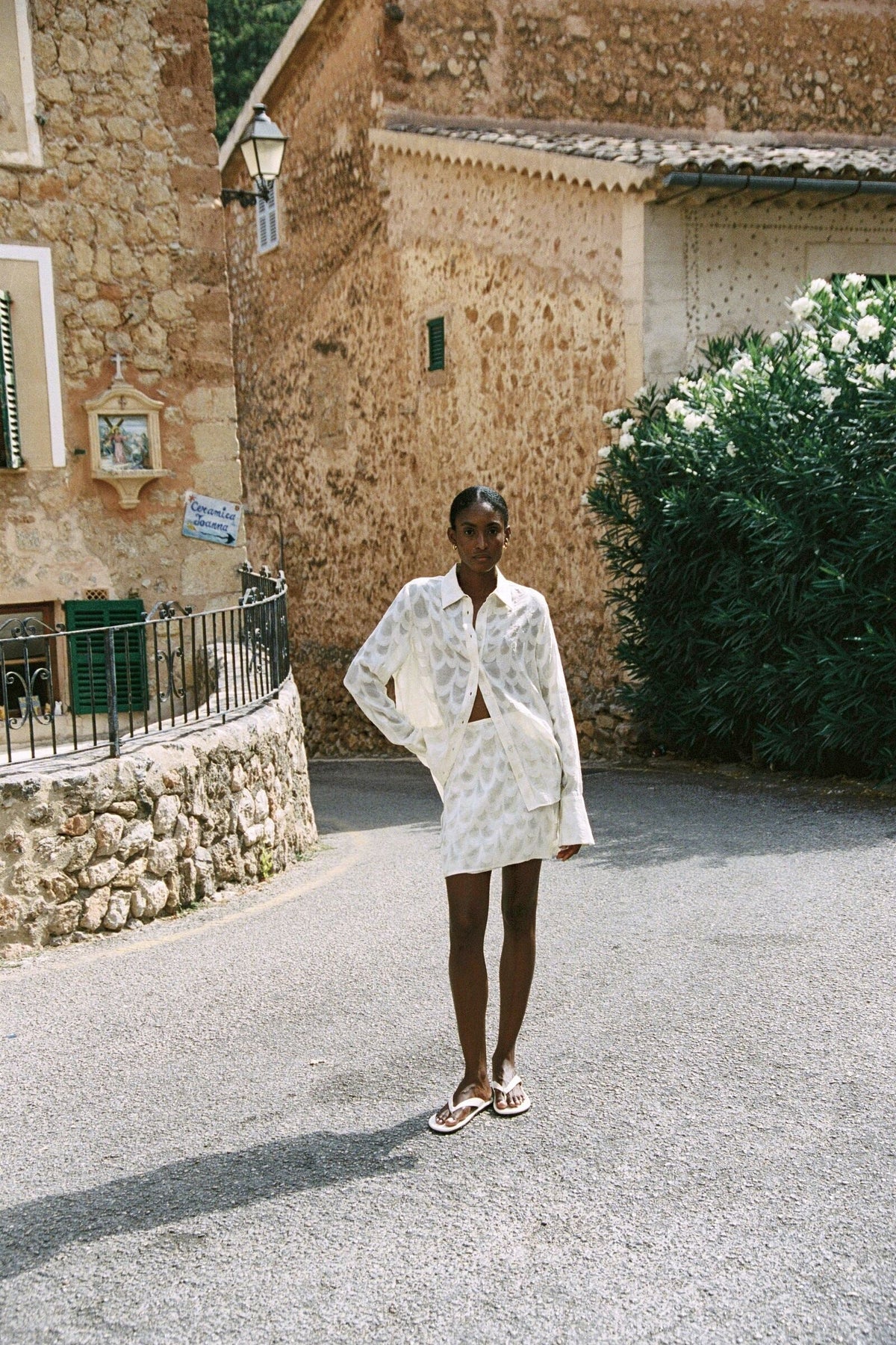 Model wearing the AUDĒRE. Rae semi-sheer shirt in Ivory, full-length view walking in a stone lane.