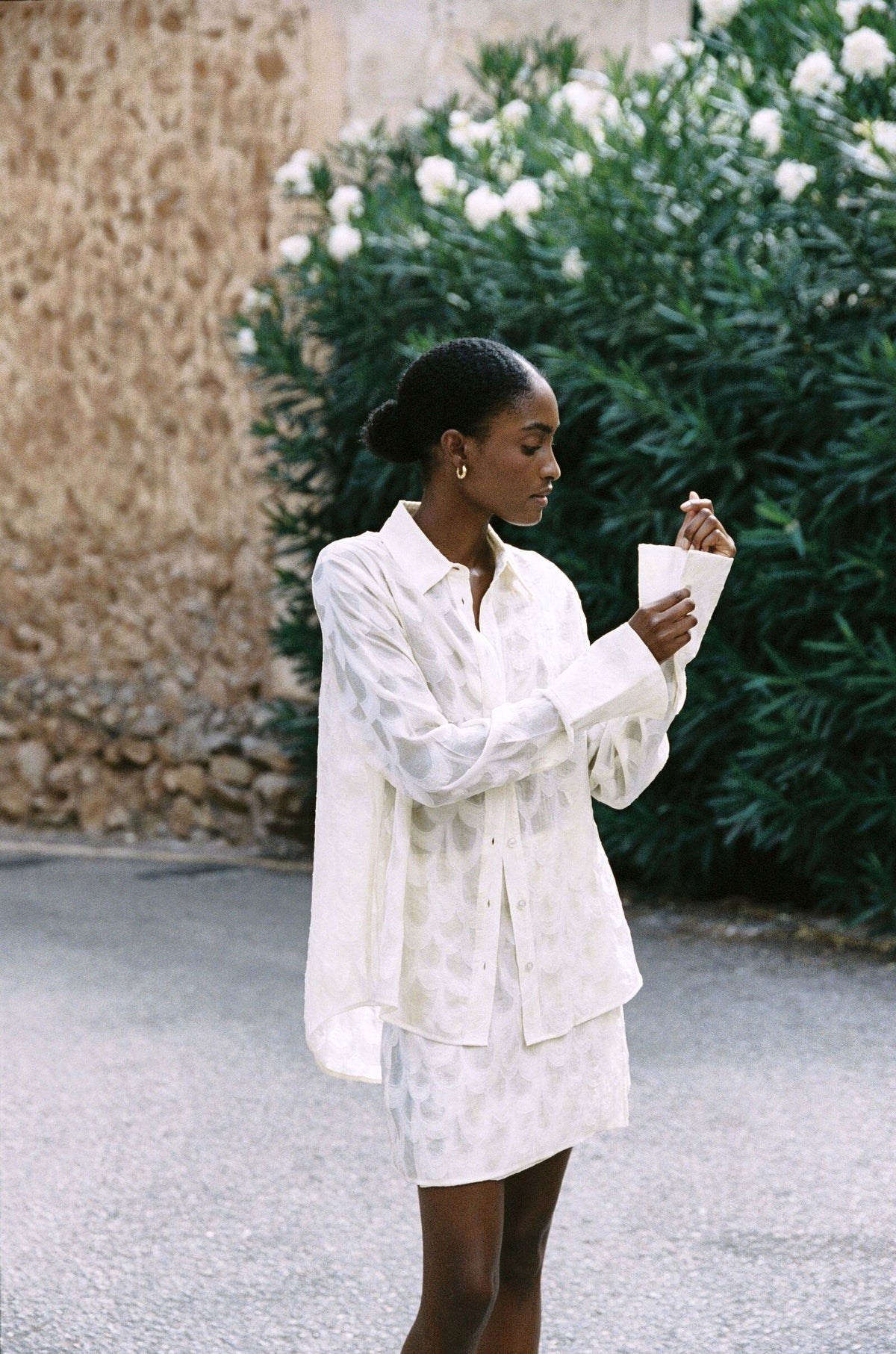 Model wearing the AUDĒRE. Rae semi-sheer shirt in Ivory, front view while adjusting a cuff.