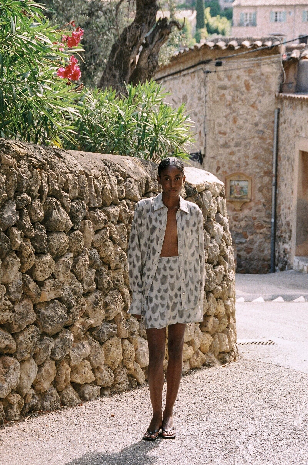 Model wearing the AUDĒRE. Rae wrap mini skirt in Dove, full-length view beside a stone wall.