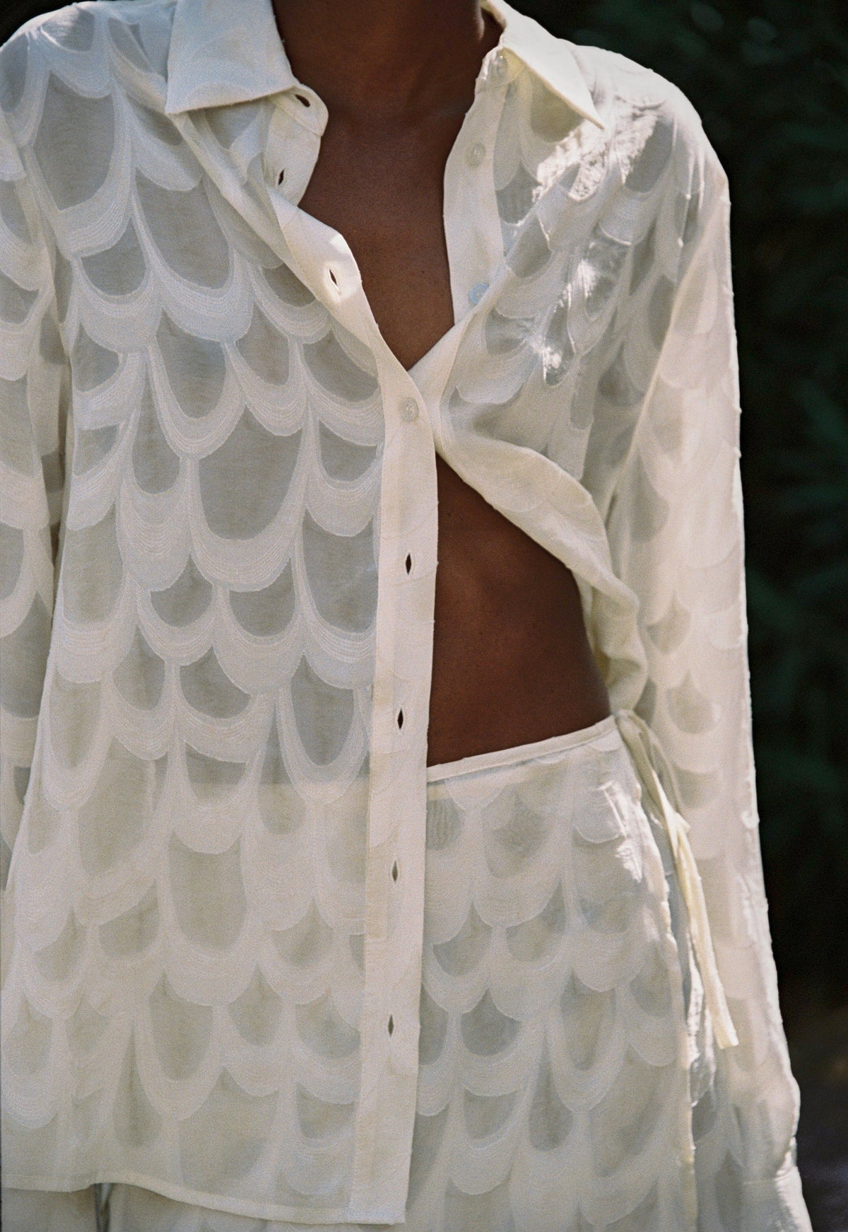 Model wearing the AUDĒRE. Rae wrap mini skirt in Ivory, close-up of the wrap skirt and shirt fabric.